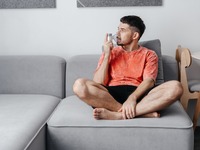 Ein Mann, der auf einem Sofa sitzt und inhaliert. Das Bild zeigt einen Mann, der auf einem Sofa sitzt und inhaliert.