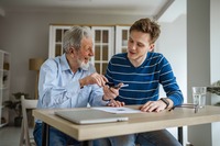 Ein älterer Mann, der mit einem jungen Mann an einem Tisch sitzt. Das Bild zeigt einen älteren Mann, der mit einem jungen Mann an einem Tisch sitzt.