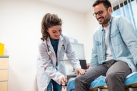Eine Ärztin untersucht das Knie von einem Mann. Das Bild zeigt eine Ärztin, die das Knie von einem Mann untersucht.