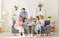 Ein Großvater, der auf dem Sofa sitzt und mit seinen Kindern und Enkelkindern ein Buch anschaut. Ein Großvater, der auf dem Sofa sitzt und mit seinen Kindern und Enkelkindern ein Buch anschaut.