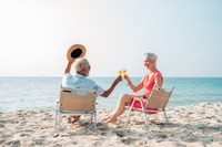 Ein älterer Mann und eine ältere Frau, die in Liegestühlen am Strand sitzen und anstoßen. Das Bild zeigt einen älterer Mann und eine ältere Frau, die in Liegestühlen am Strand sitzen und anstoßen.