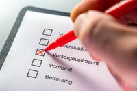 Jemand setzt ein Kreuz auf einem Papier, neben Vorsorgevollmacht